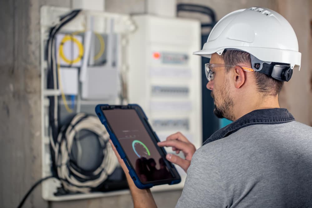un professionnel qui tient une tablette devant un tableau électrique pour un auditi énergétique maison