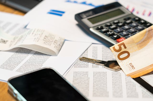 un billet de 50Euros, une calculatrice et un téléphone portable posé sur une pile de papiers, rénovation cuisine