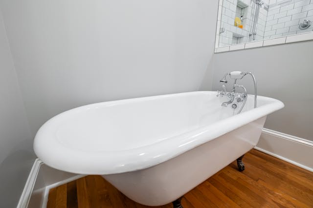 une baignoire ilôt das une salle de bain avec parqsuet en bois et murs gris