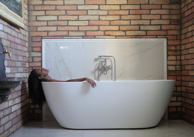une femme dans une baignoire ilôt, entre des murs en brique.
