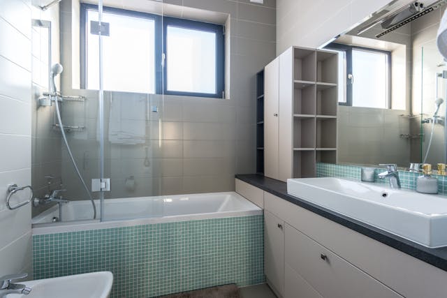 une douche baignoire avec du carrelage vert et blanc, avec ue vasque xxl, un miroir et un rangement sur le côté, douche remplacement baignoire